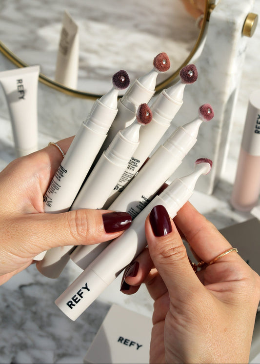Hands holding multiple REFY skincare products with a blurred background